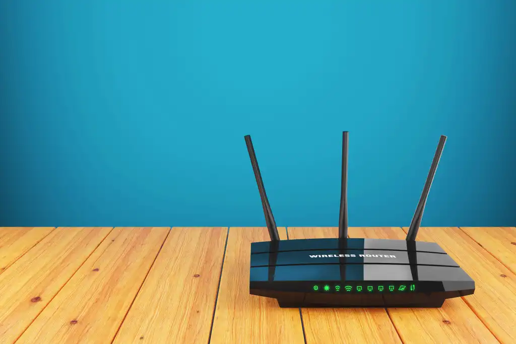 Stock photo of a wireless router sitting on a wood table with a plain blue wall behind them