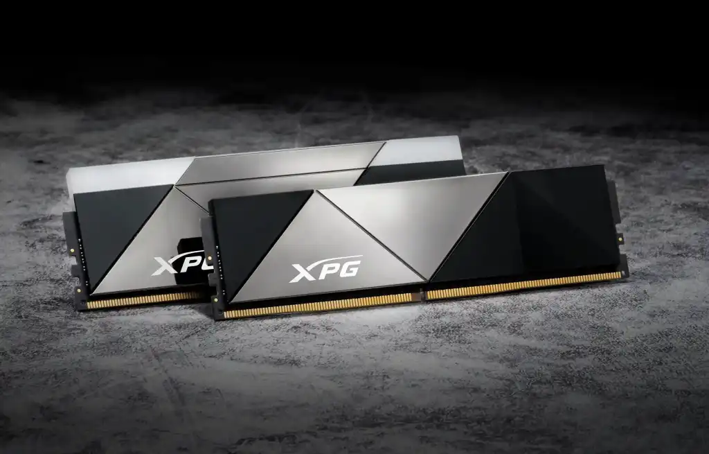 Photo of two XPG branded RAM sticks in a spotlight, sitting on a textured grey surface